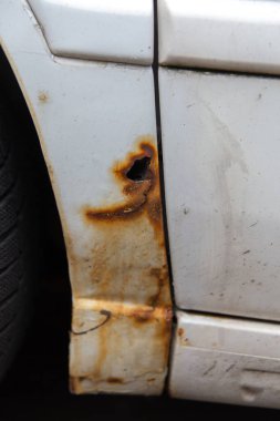 Beyaz eski arabanın yan tarafında pas var. Eski, yıpranmış metal yüzeydeki pas deliği..