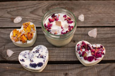 Gül yapraklı mum ve vida kapaklı bir kavanozda yarı değerli gül kuvars taşları ve üç kalp şeklinde mum. Yukarıdan görüntüle