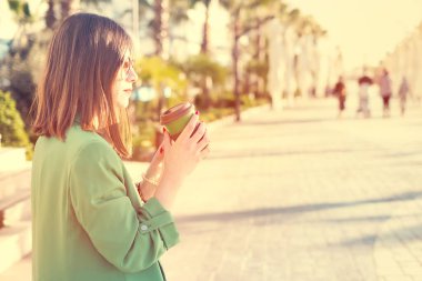 Dışarıda elinde bambu kahve kupası tutan bir kadın var. Yüksek kaliteli fotoğraf. Sıcak güneş parlıyor.