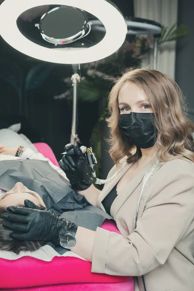 Kozmetik uzmanı bir müşteri için kalıcı makyaj kaşları uyguluyor.