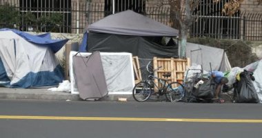 Los Angeles, CA USA - 1 Ekim 2021: Lüks bir apartman binasının önündeki kampı süpüren evsiz adam