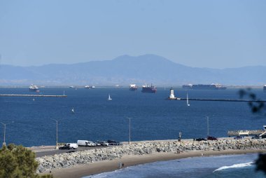 Yelkenli, Los Angeles Limanı 'ndaki deniz fenerinden geçiyor. Konteynır gemileri denizde bekliyor.
