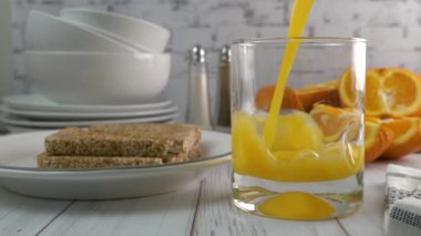 Bir tabak tostun yanına portakal suyu döküyorum. Çok yavaş.