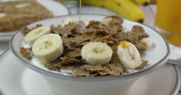 用牛奶和香蕉把蜂蜜倒在一碗有机麸皮上 — 图库视频影像