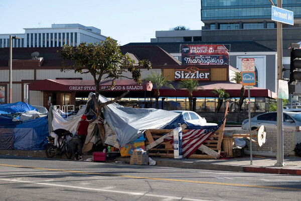 Los Angeles, CA USA - Novmber 14, 2021:  Homeless encampment in front of a Sizzler restaurant with a banner promoting Thanksgiving dinner special