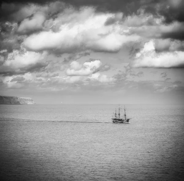 Tall sailing ship on open sea, in black and white with clifs in background