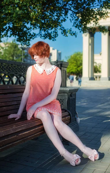 夏天的一天 穿着粉色短裙的漂亮红头发姑娘坐在公园的长椅上 — 图库照片