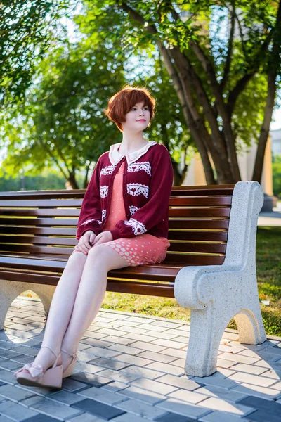 Красивая Рыжая Девушка Коротком Розовом Платье Скамейке Парке Летний День — стоковое фото