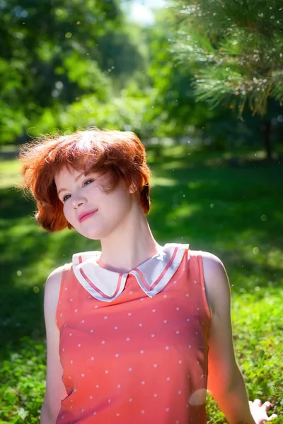 Yeşil yaprakların arasına park etmiş kızıl saçlı mutlu bir kızın portresi..
