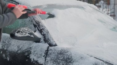 Bir adam arabadaki karı temizler. Adam kışın sokakta arabasındaki karları temizler.