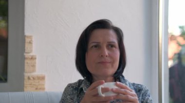 Mutlu kadın evde bir fincan sıcak çay ya da kahveyle dinleniyor.