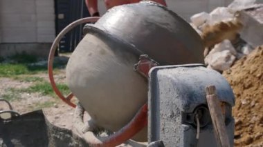 Küçük inşaat alanındaki kum yığınının yanında eski kirli beton karıştırıcı. Evde küçük taşınabilir çimento karıştırma makinesi. İnşaat alanı