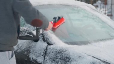 Bir adam arabadaki karı temizler. Adam kışın sokakta arabasındaki karları temizler.