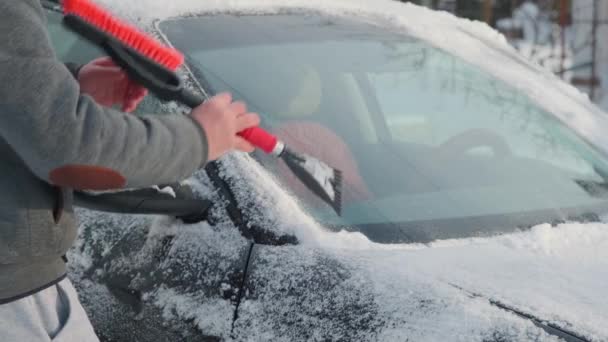 Um homem limpa a neve do carro. Homem limpa neve de seu carro na rua no inverno — Vídeo de Stock