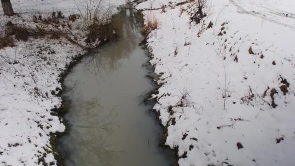 Zimní řeka. Špinavá voda vstupuje do říčního kanálu potrubím. Písečné dole. — Stock video
