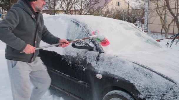 Чоловік розчищає сніг від машини. Чоловік розчищає сніг зі своєї машини на вулиці взимку — стокове відео
