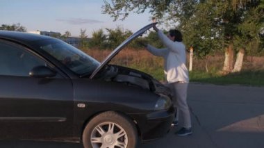 Kadın kırılan arabanın kaputunu açar ve motora bakar.