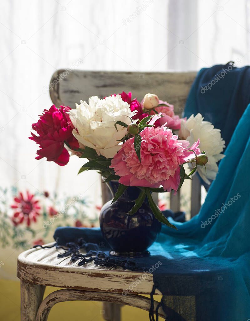 Still life with white and pink peonies in a blue vase on vintaje chair