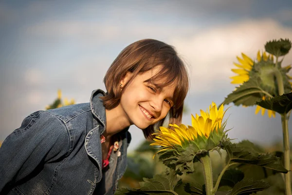 Liten flicka luktar solrosor i fält — Stockfoto