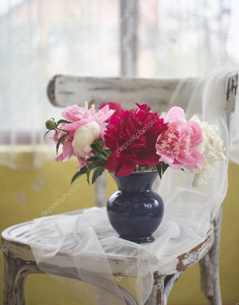 Still life with white and pink peonies in a blue vase on vintaje chair