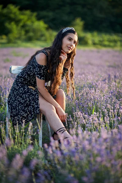 漂亮的女孩穿着一件布克的衣服坐在一张木椅上 在薰衣草地中间摆姿势 — 图库照片