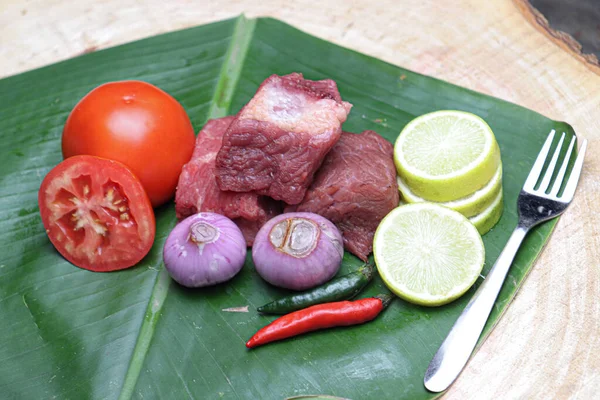 fresh tasty cow beef with sliced lemon and tomato on banana leaf