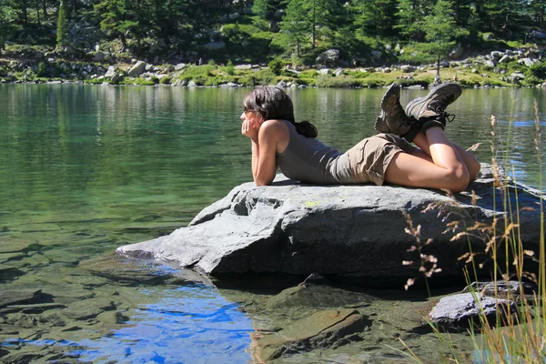 Девушка-путешественница на камне, голодающая на озере — стоковое фото