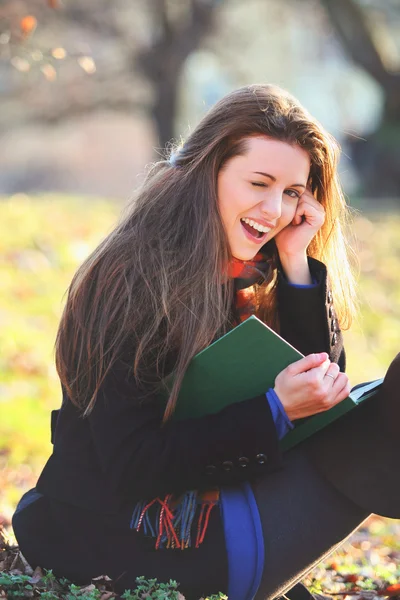 Joyful and smiling girl reading a book in the park — Stock Photo, Image