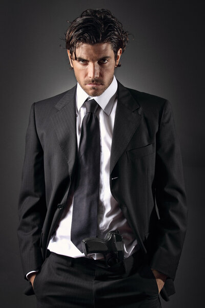 Привлекательный и элегантный мужчина позирует с пистолетом в штанах

