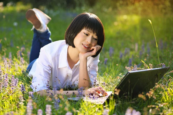 Atractiva chica asiática usando portátil entre flores —  Fotos de Stock