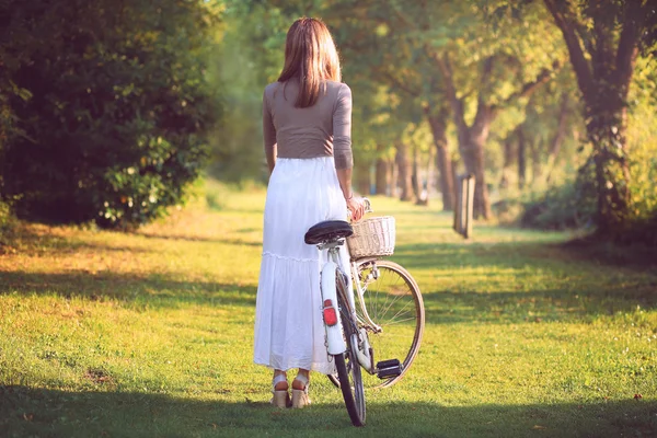 Femme avec un vélo vintage à la lumière du coucher du soleil — Photo