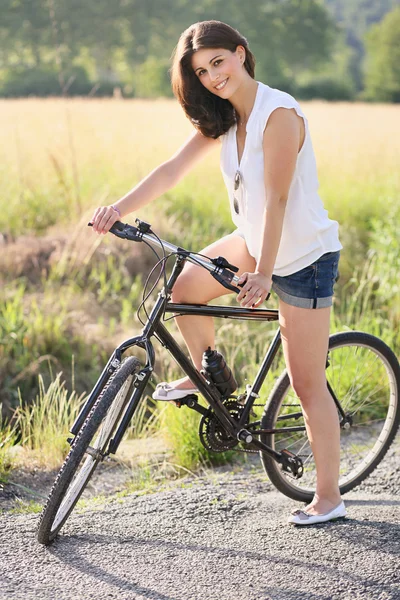 Smiling young woman with bicycle on a country road — Stock Photo, Image