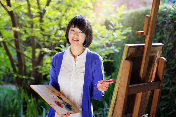 Happy young woman painting a canvas in the garden