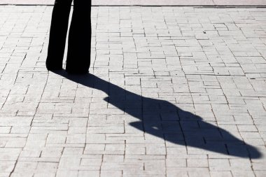 Caddede duran bir kızın gölgesi ve silueti. Kaldırımda pantolon giymiş sıska kadın bacakları, yalnızlık kavramı, dramatik bir hikaye.