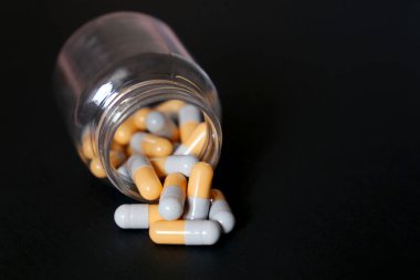 Siyah arka planda haplar, kapsüllerde bir şişe ilaç. Besleyici maddeler, vitaminler, antidepresanlar kavramı