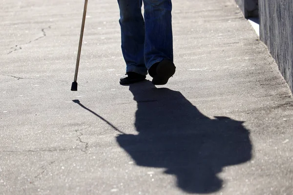 一个人走在街上拿着手杖 在沥青路面上的影子 脊柱疾病或关节疾病 老年人的概念 — 图库照片