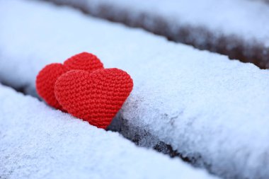 Parktaki bankta karda örülmüş kırmızı kalpler. Sevgililer günü kartı, iki aşk sembolü, kışın romantik etkinlik için arka plan, Noel kutlaması.