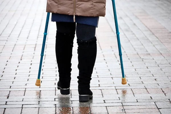 Woman walking with crutches on a city street, female legs on sidewalk. Concept of disability, limping person with injury