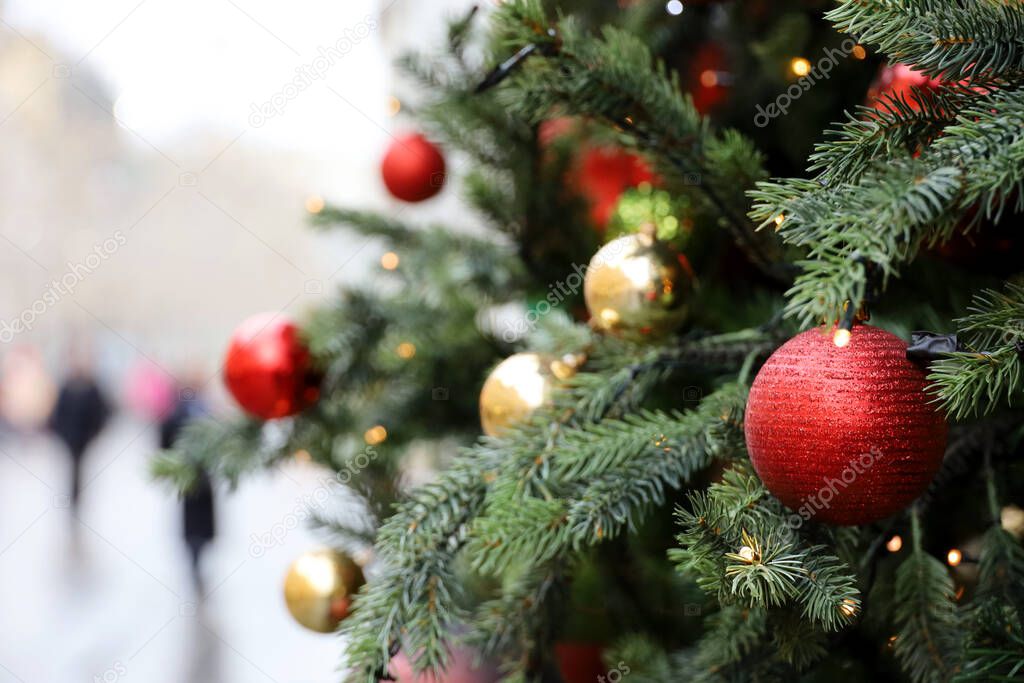New Year decorations on a city street. Christmas tree with red and golden toy balls on blurred people background