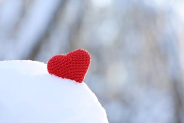 Red knitted heart in snow on winter forest background. Valentine's card, romantic love