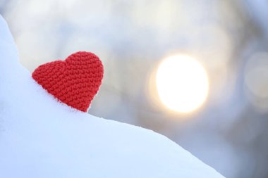 Red knitted heart in snow on winter sun background. Valentine's card, romantic love