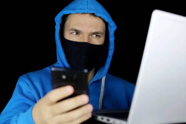 Man Mask Blue Hoodie Sitting Smartphone Hand Laptop Black Background —  Fotos de Stock