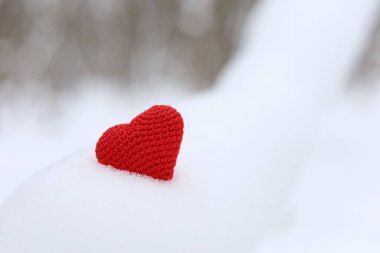 Red knitted heart in snow on winter forest background. Valentine's card, romantic love