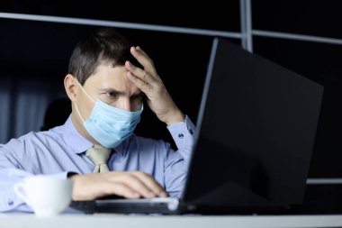 Yüz maskesi ve ofis kıyafetleri giymiş endişeli bir adam dizüstü bilgisayar ekranına bakıyor. Zor bir görevi çözme kavramı
