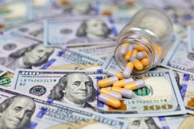 Kapsüllerdeki haplar bir şişeden Amerikan dolarına saçılmış. ABD 'de sağlık hizmeti kavramı, ilaç ticareti, uyuşturucu fiyatları, eczane, tıp ve ekonomi