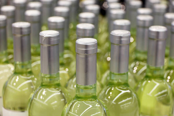 Бутылки белого вина подряд, избирательный фокус. Винный магазин, производство вина