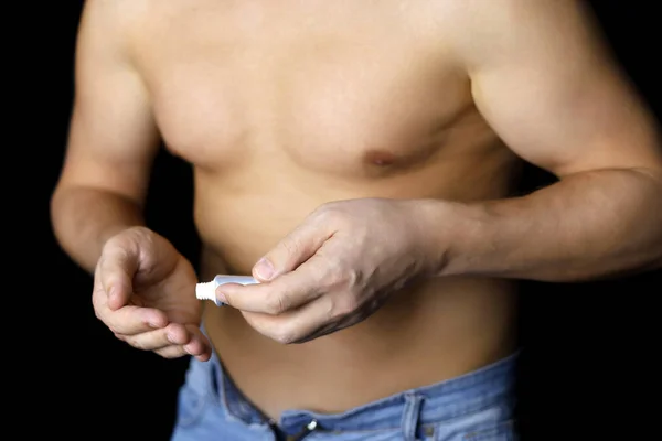 Man Jeans Naked Torso Applies Cream Tube Hand Black Background — Stock Photo, Image