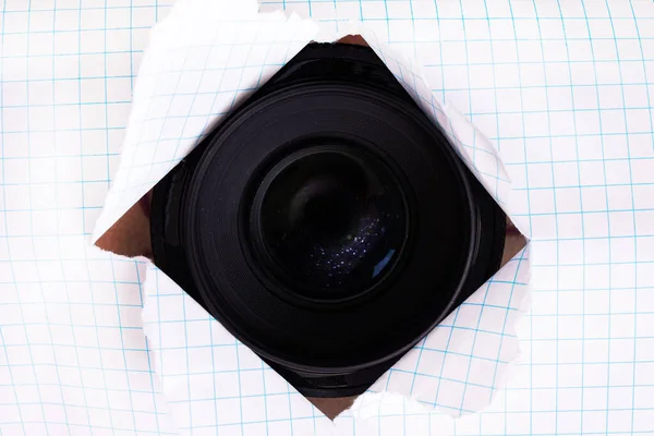 Lente da câmera em um furo rasgado no papel — Fotografia de Stock