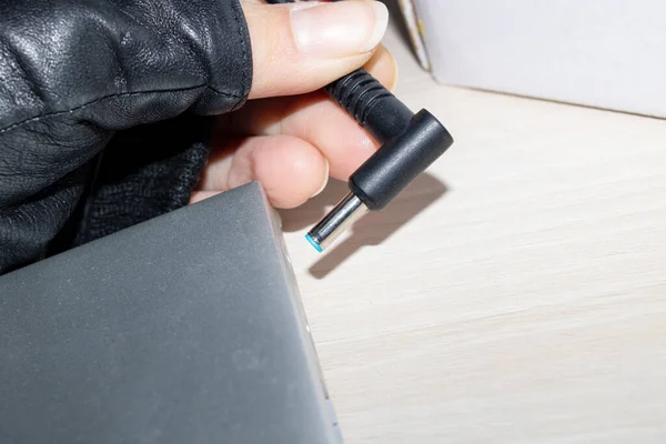 Рука вставляє зарядний пристрій у ноутбук на дерев'яному столі — стокове фото