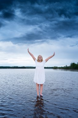 young woman standing on a lake with a powerful storm behind her clipart